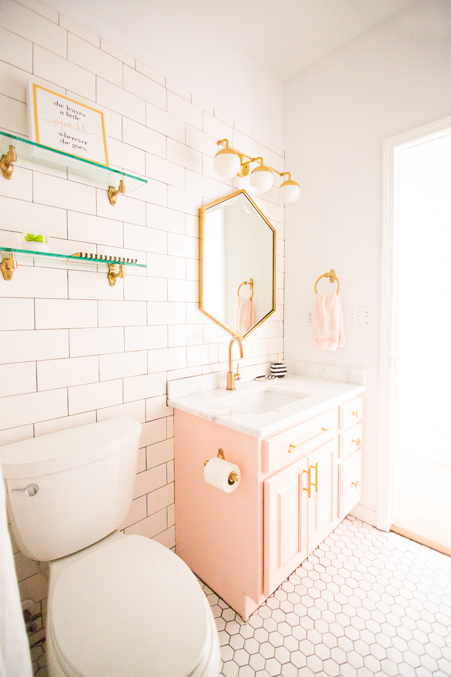 Modern Glam Blush Girls Bathroom Design gold hexagon mirror blush cabinets gold hardware white hexagon floor glass shelves pink bathroom cabinets gold orb sconce-1-3