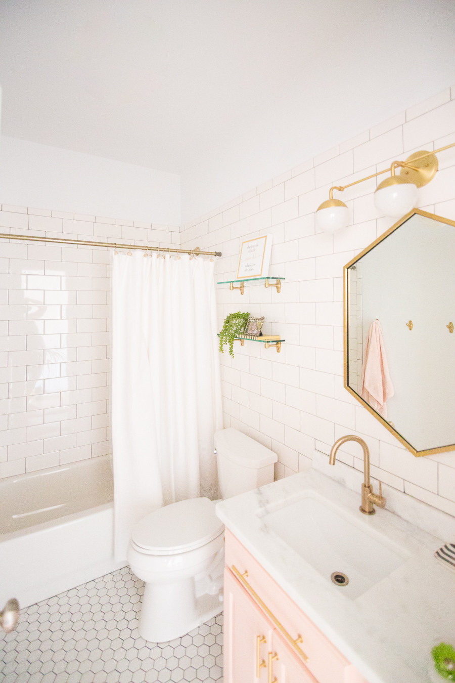 Modern Glam Blush Girls Bathroom Design gold hexagon mirror blush cabinets gold hardware white hexagon floor glass shelves pink bathroom cabinets gold orb sconce-1-3