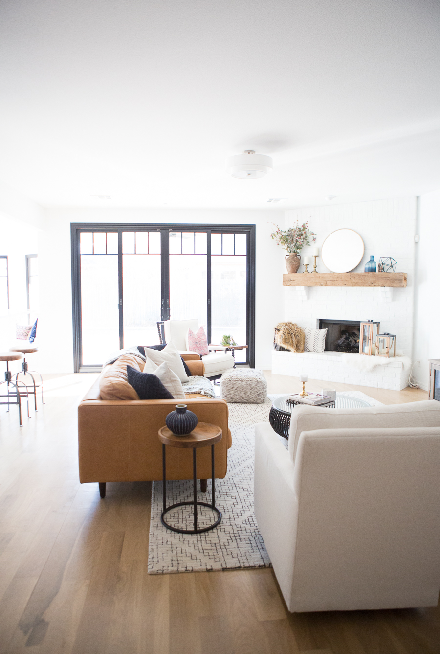 Tulsa Remodel Reveal Modern White Farmhouse black windows and doors modern leather sofa article Sven sofa white brick fireplace wood beam mantle round gold mirror tv gallery wall-1-2