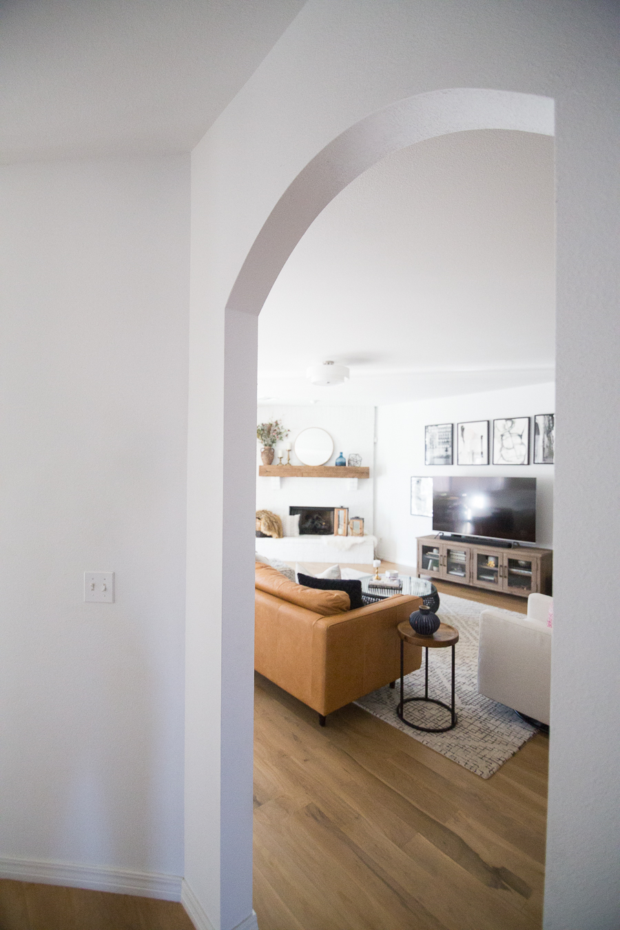 White Painted Brick Fireplace Makeover TV collage wall pottery barn wood media console article sven leather sofa faux fiddle leaf fig tree wood lanterns round gold mirror fireplace styling white walls black windows