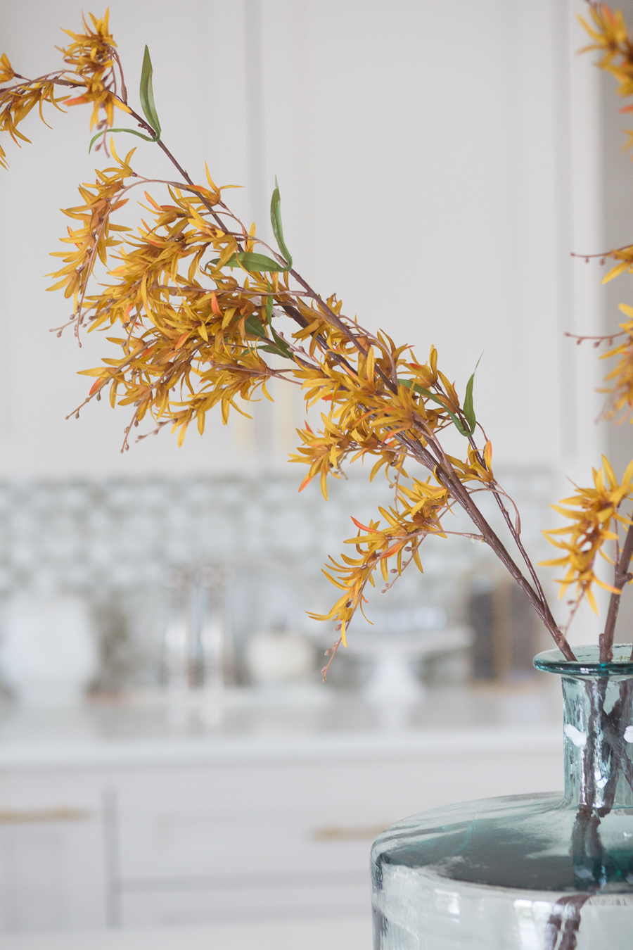 Loveliest Looks of Fall Home Tour Beautiful Fall Home Decor and Fall Fashion Ideas close up photo of yellow faux fall stems in a green vase sitting on a large quartzite waterfall kitchen countertop