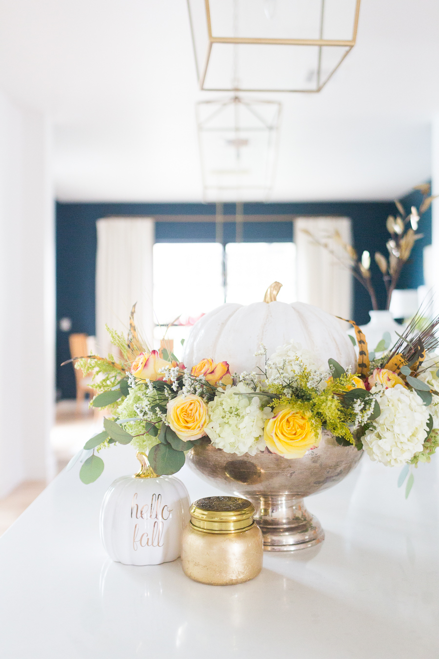 DIY Silver Urn Pumpkin Centerpiece for Fall hydrangeas and eucalyptus and roses inside of a silver urn with a ceramic pumpkin for a Thanksgiving centerpiece sitting beside a fall Anthropologie candle and hello fall pumpkin