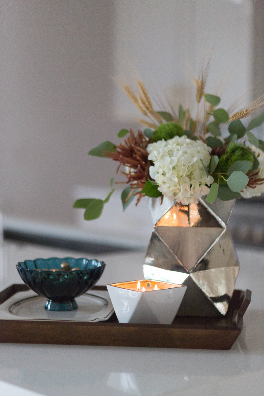 Simple Ways to Decorate for the Holidays from West Elm large wood tray faceted silver vase with hydrangeas and fall flower arrangement scented candle quartz waterfall countertops with gold bar stools