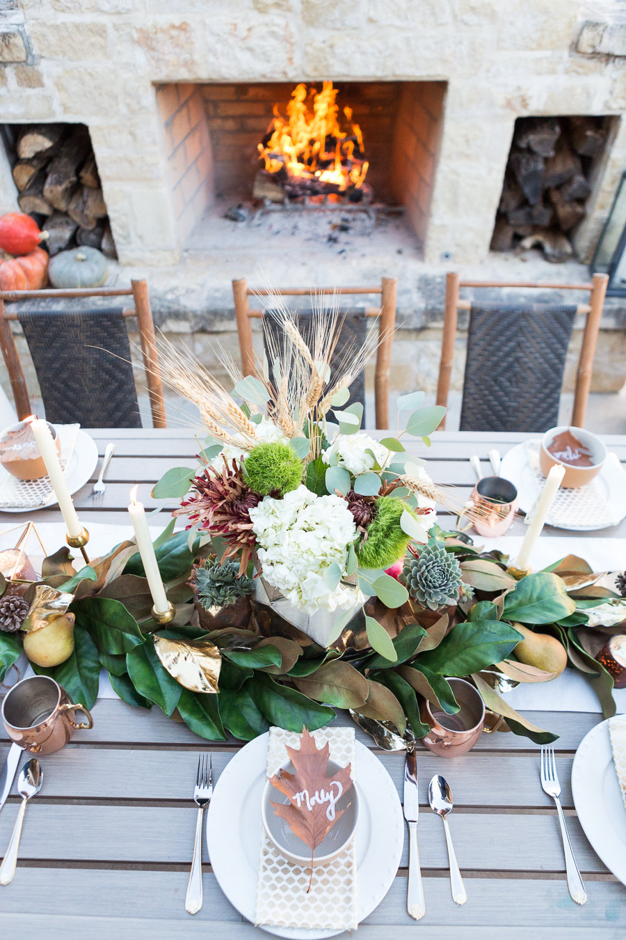 Simple Ways to Decorate for the Holidays from West Elm outdoor Friendsgiving and thanksgiving tablescape magnolia garland with gold candlesticks and a rock outdoor fireplace and copper votive candles