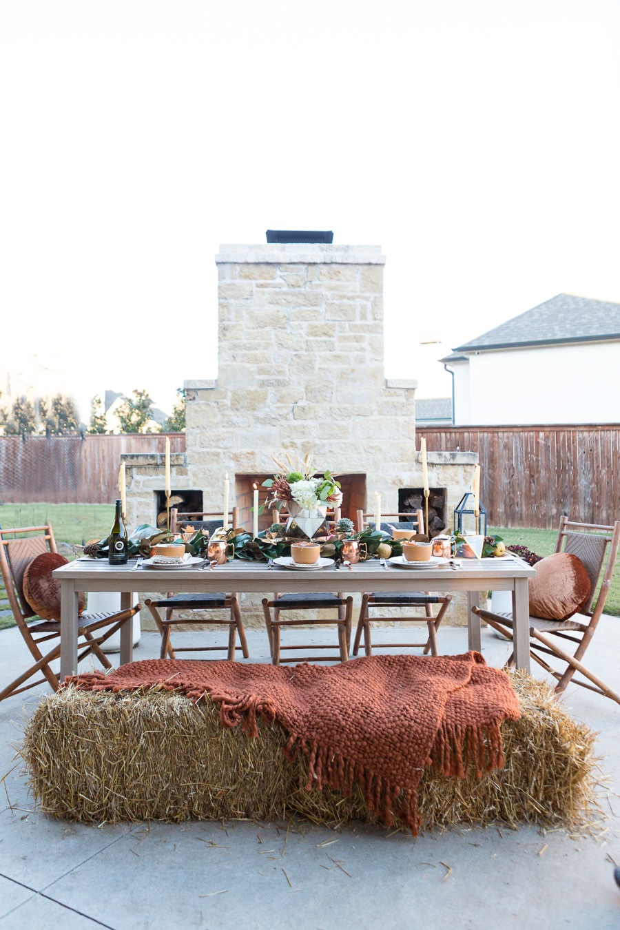 Simple Ways to Decorate for the Holidays from West Elm outdoor Friendsgiving and thanksgiving tablescape magnolia garland with gold candlesticks and a rock outdoor fireplace and copper votive candles hay bail with a chunky knit throw and copper velvet pillows