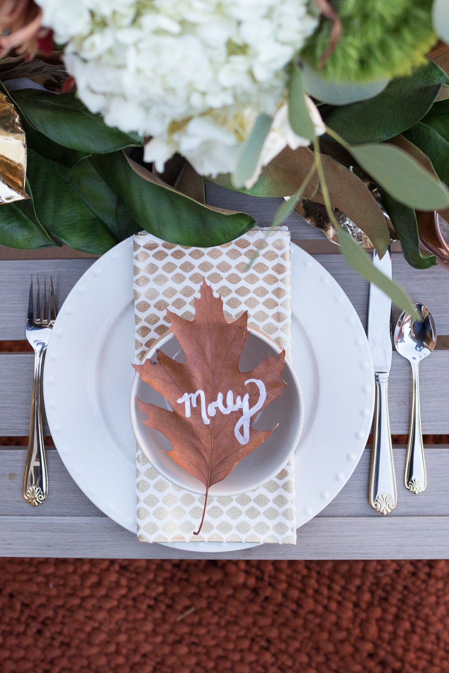 Simple Ways to Decorate for the Holidays from West Elm outdoor Friendsgiving and thanksgiving tablescape magnolia garland with gold candlesticks and a rock outdoor fireplace and copper votive candles hay bail with a chunky knit throw and copper velvet pillows