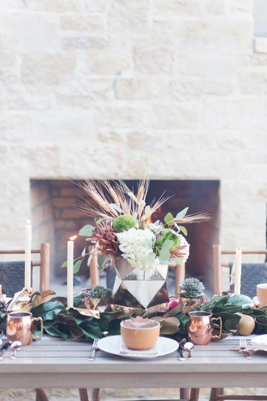 Simple Ways to Decorate for the Holidays from West Elm outdoor Friendsgiving and thanksgiving tablescape magnolia garland with gold candlesticks and a rock outdoor fireplace and copper votive candles hay bail with a chunky knit throw and copper velvet pillows