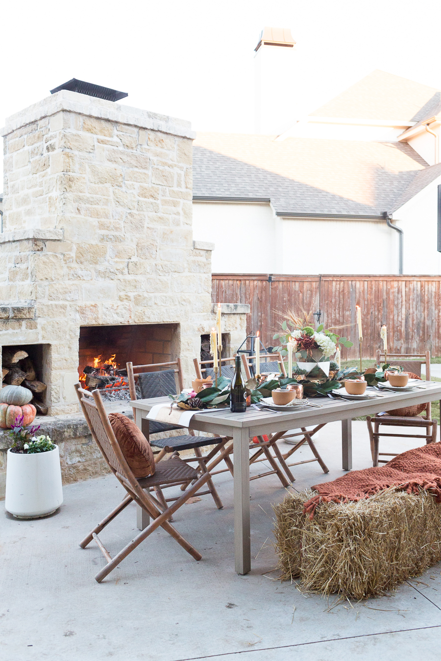 Simple Ways to Decorate for the Holidays from West Elm outdoor Friendsgiving and thanksgiving tablescape magnolia garland with gold candlesticks and a rock outdoor fireplace and copper votive candles hay bail with a chunky knit throw and copper velvet pillows