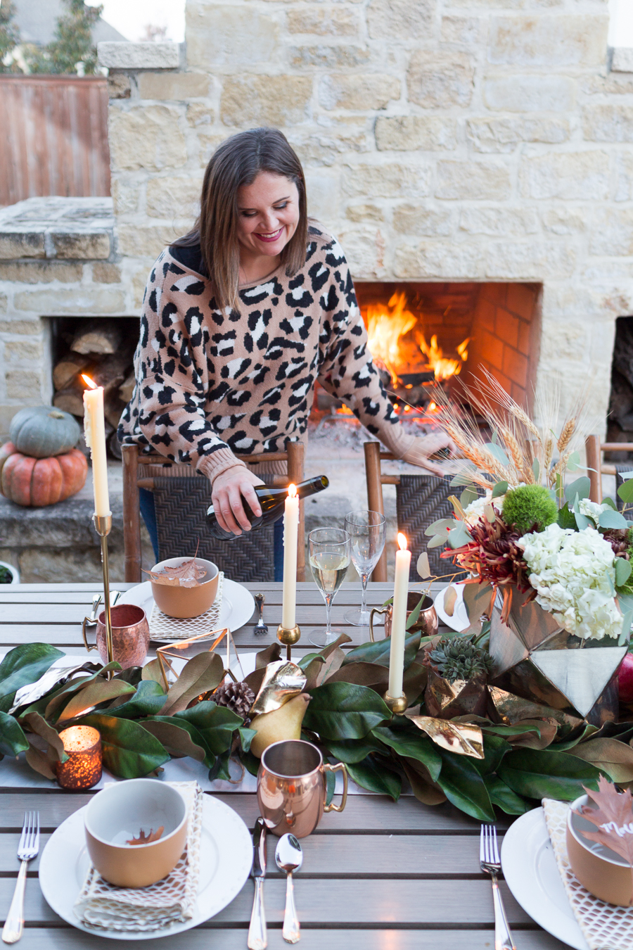 Simple Ways to Decorate for the Holidays from West Elm outdoor Friendsgiving and thanksgiving tablescape magnolia garland with gold candlesticks and a rock outdoor fireplace and copper votive candles hay bail with a chunky knit throw and copper velvet pillows