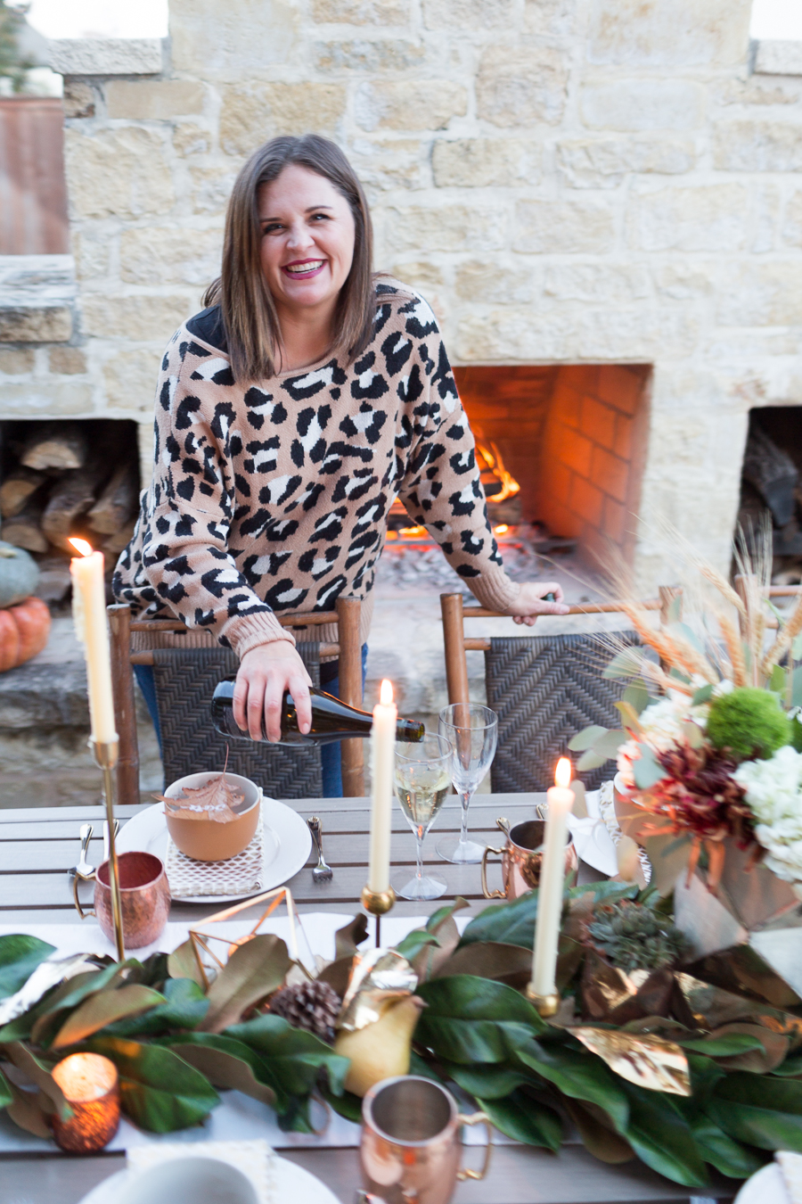 Simple Ways to Decorate for the Holidays from West Elm outdoor Friendsgiving and thanksgiving tablescape magnolia garland with gold candlesticks and a rock outdoor fireplace and copper votive candles hay bail with a chunky knit throw and copper velvet pillows