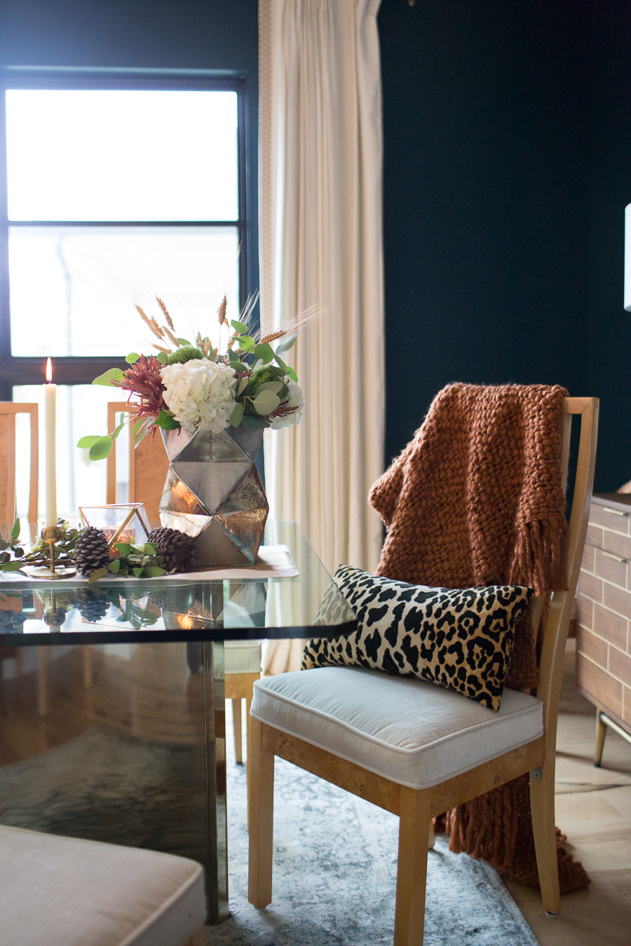 Simple Ways to Decorate for the Holidays from West Elm dark green painted dining room with glass and gold marble dining room table and burl wood chairs with a holiday tablescape with gold candlesticks and a large silver faceted vase with fresh flowers