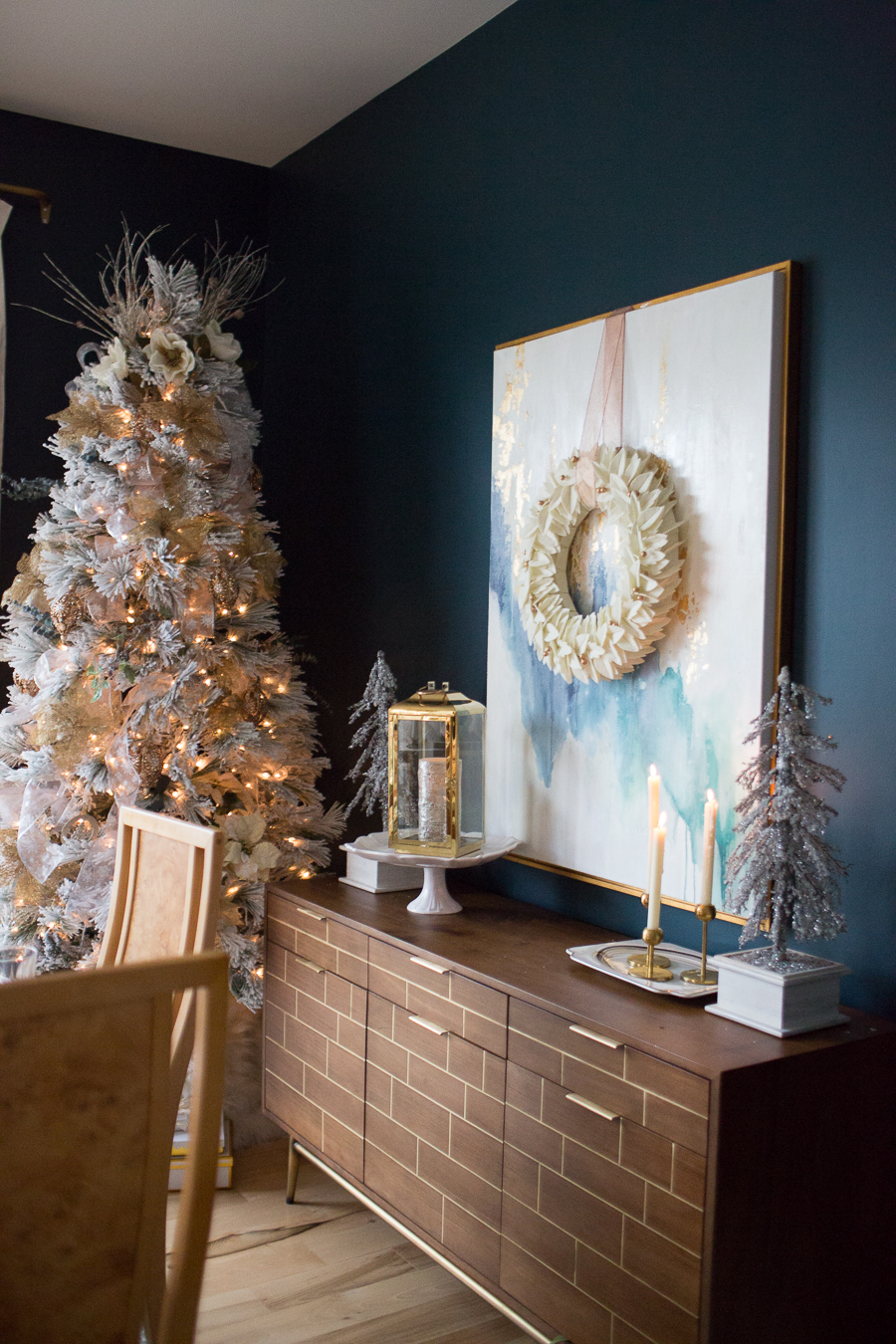 Budget Friendly Holiday Decor from Walmart wood tray with a gold lantern and pioneer woman white cakestand on top of a large quartz waterfall island Christmas tree in a dark blue green dining room with an abstract painting hanging on the wall