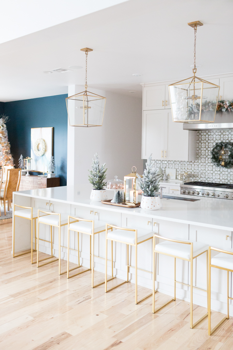 Budget Friendly Holiday Decor from Walmart white quartz waterfall island with gold bar stools and gold lanterns and a wood tray with a gold lantern and flocked Christmas trees in a polka dot vase