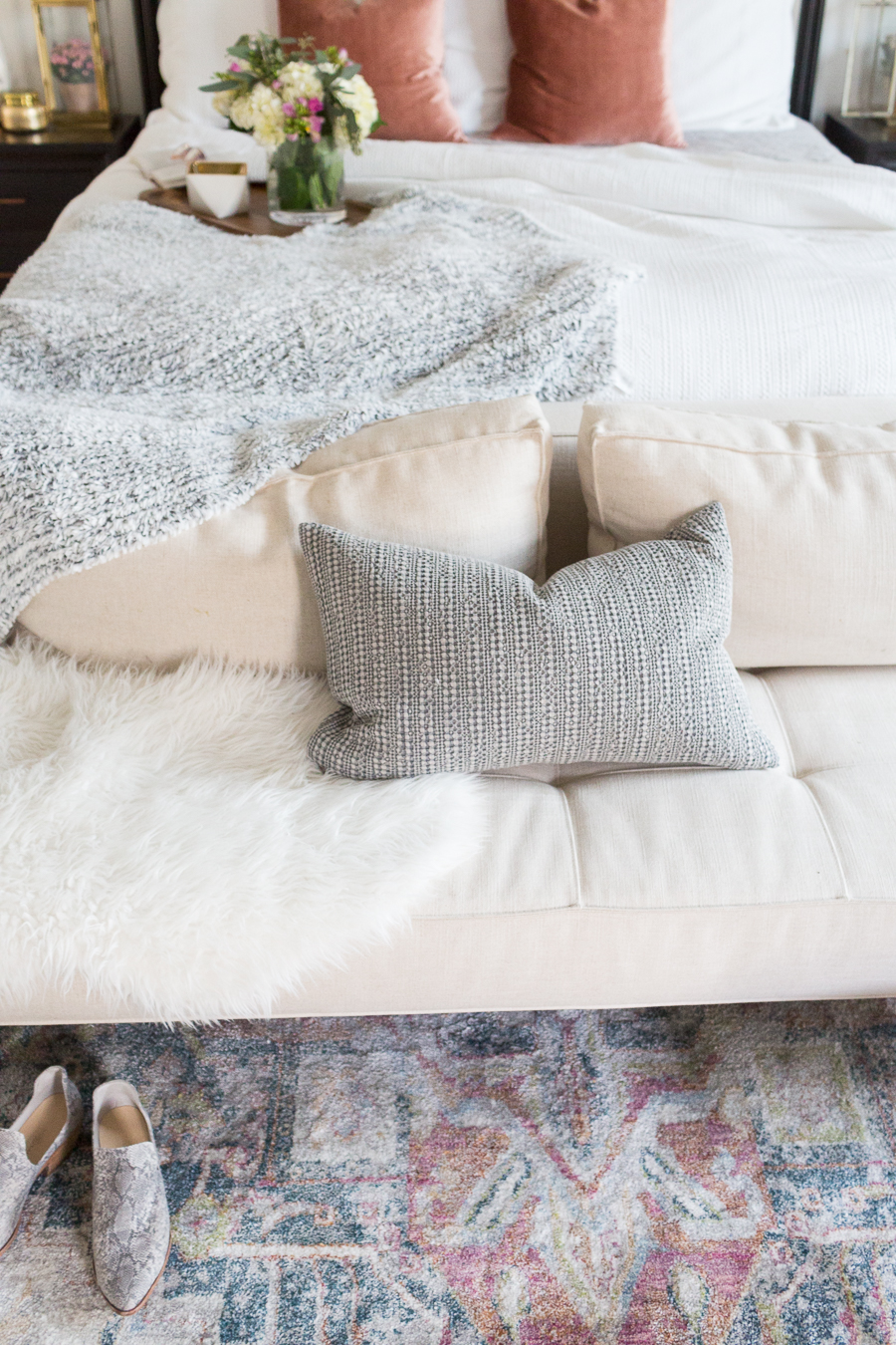 Refresh Your Master Bedroom and Bath with Pottery Barn showcasing a cream cushioned bed bench and striped pillow with snake print booties on a multi-colored faded rug