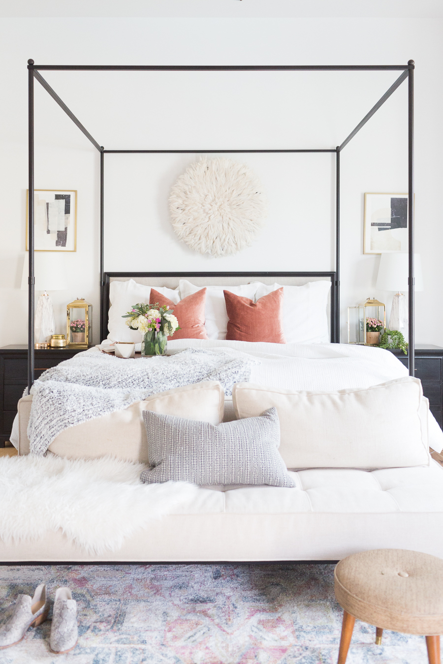 Refresh Your Master Bedroom and Bath with Pottery Barn bedroom with whites and pastel colored decor, black end tables, a black canopy bed, and faded multi-colored rug