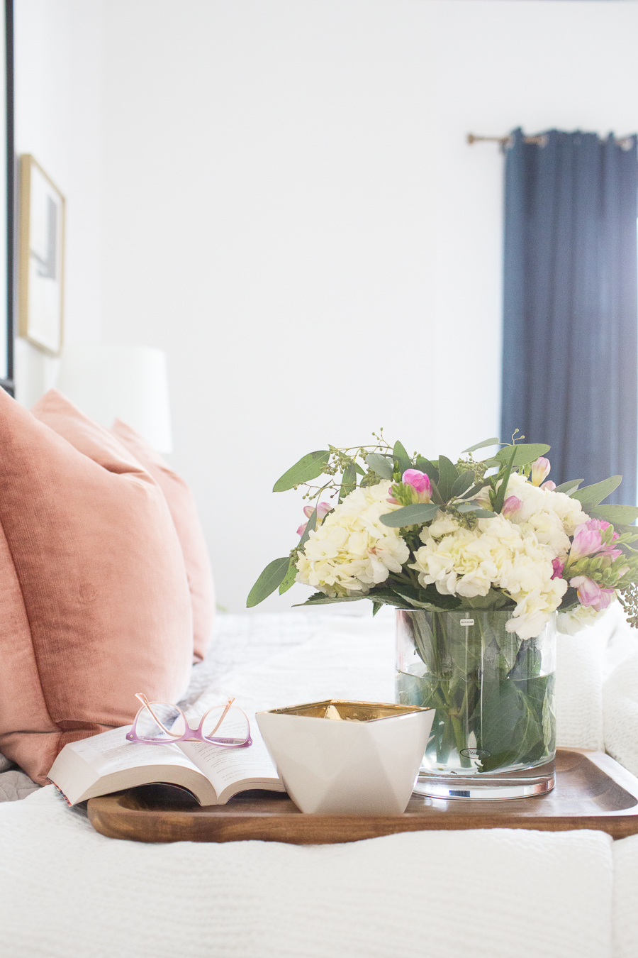 Refresh Your Master Bedroom and Bath with Pottery Barn beautiful floral arrangement on top of a wooden tray with a book open and reading glasses on a bed