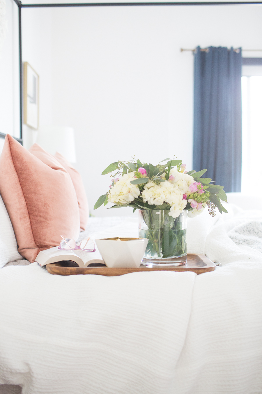Refresh Your Master Bedroom and Bath with Pottery Barn floral arrangement on wooden tray with an open book and reading glasses sitting on white bedding