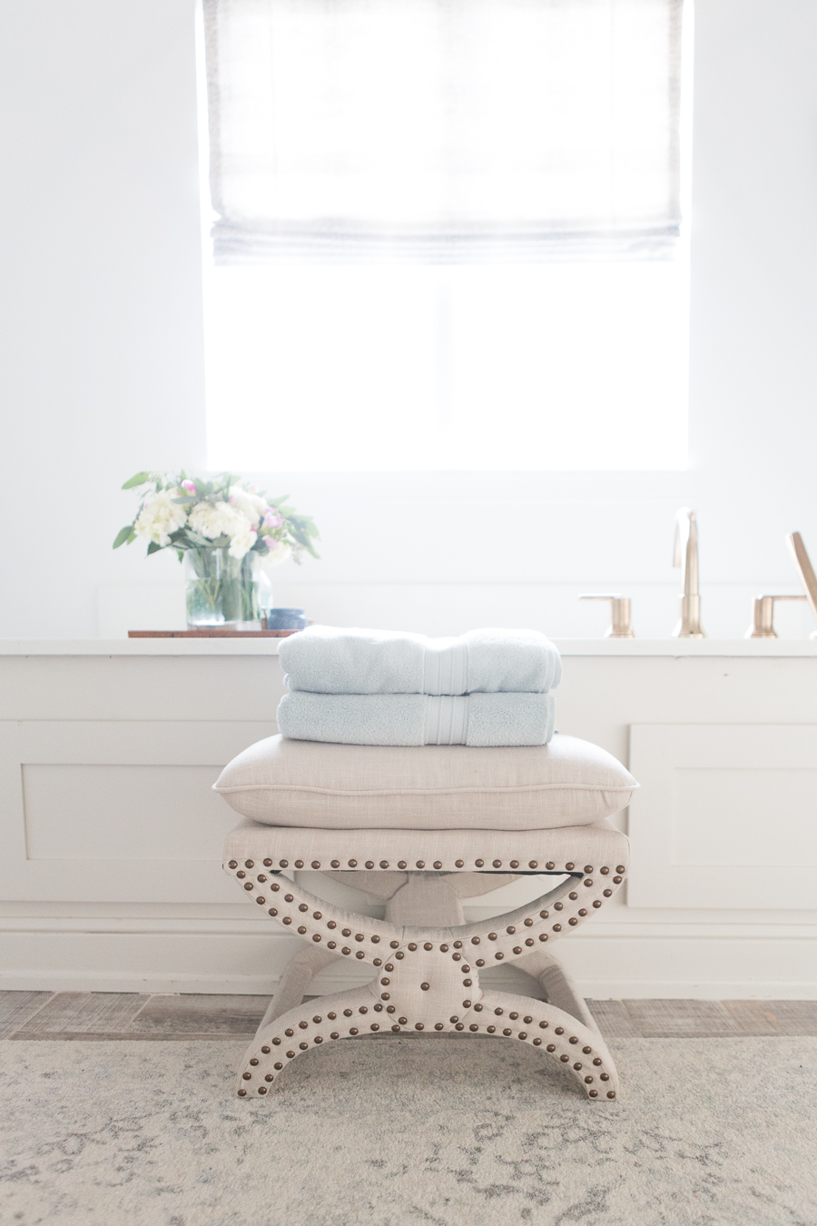 Refresh Your Master Bedroom and Bath with Pottery Barn featuring a faded blue and cream rug with a cream studded stool and powder blue towels
