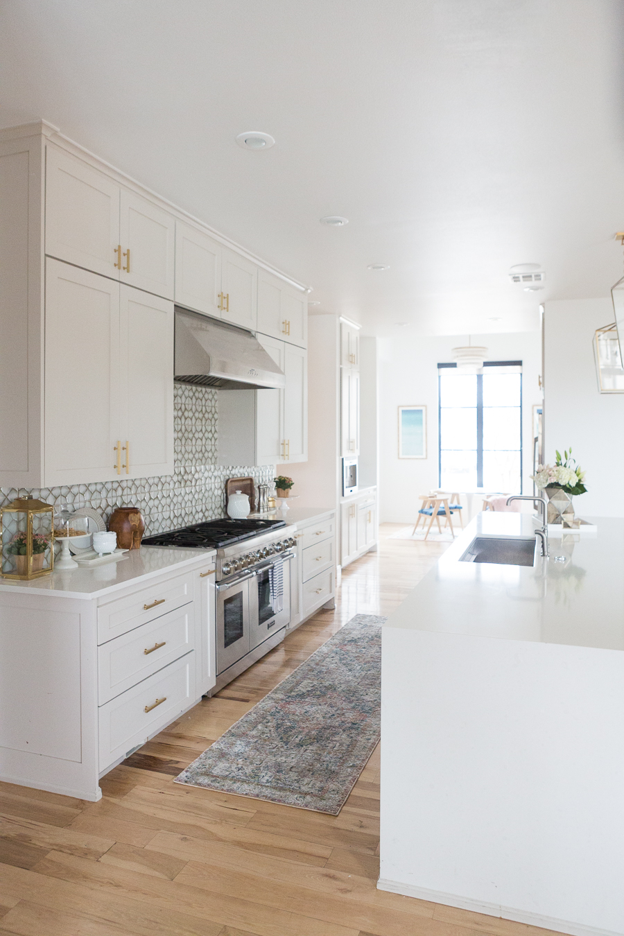 10 Beautiful Kitchen Runners for Your Home wooden floors in white kitchen with white cabinets and countertops with a geometric backsplash and golden accents