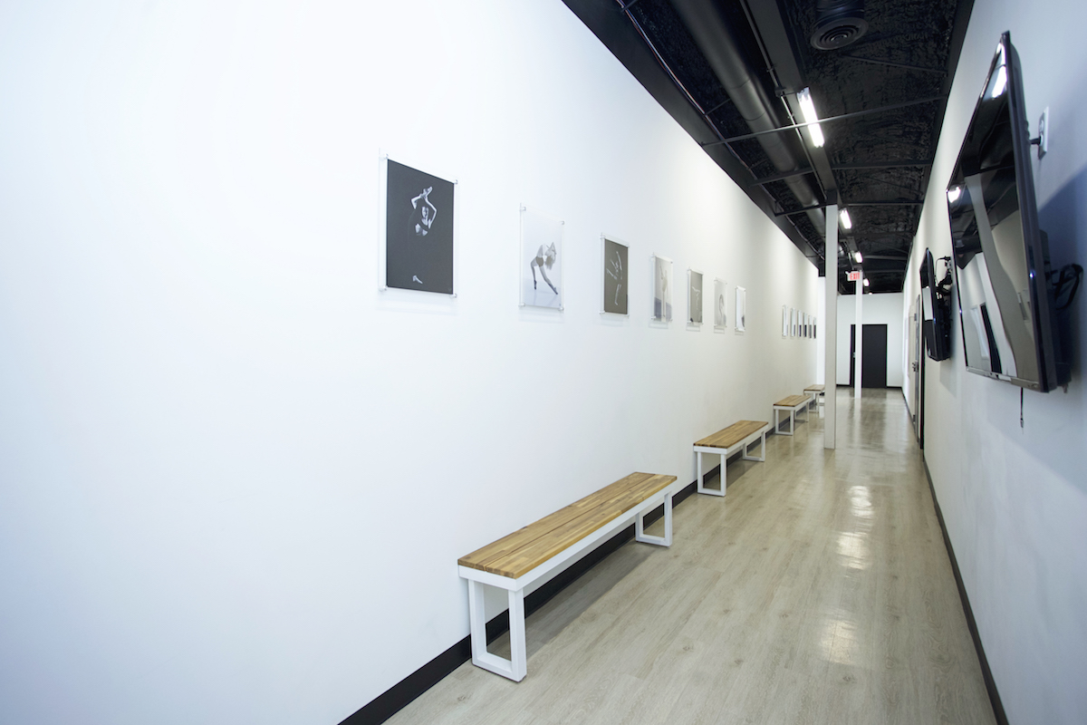 elite dance studio hallway with wooden benches, white walls and black and white photography with tvs