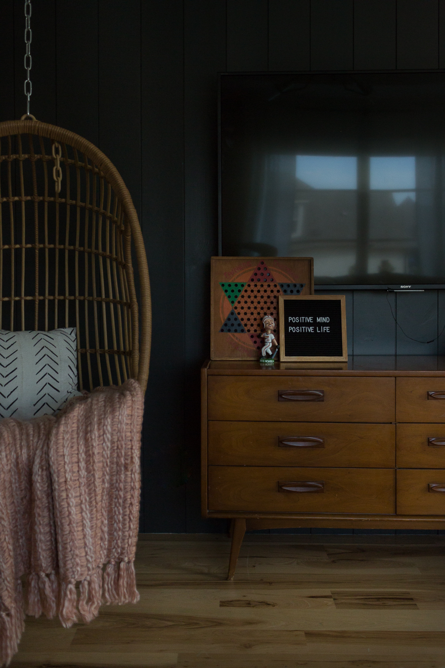 CC and Mike Teen Hangout Room Reveal with Joybird Sectional woven hanging chair against a black painted vertical shiplap wall with a midcentury modern tv stand and a letter board saying positive mind positive life blush throw african mudcloth black and white pillow