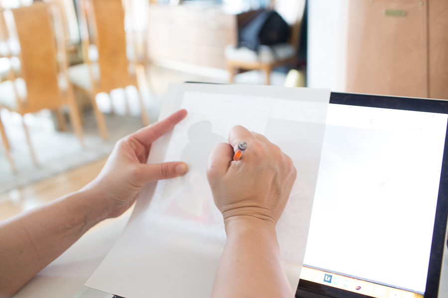 a person tracing over the laptop screen with paper and a pencil