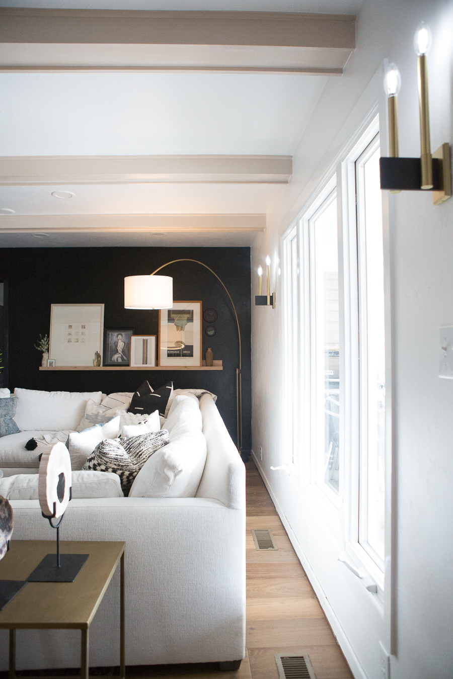 CC and Mike Kane Project Remodel Reveal white L shaped sectional on a terracotta loren rug from CC and Mike THE SHOP round coffee table black accent wall with wood art ledge