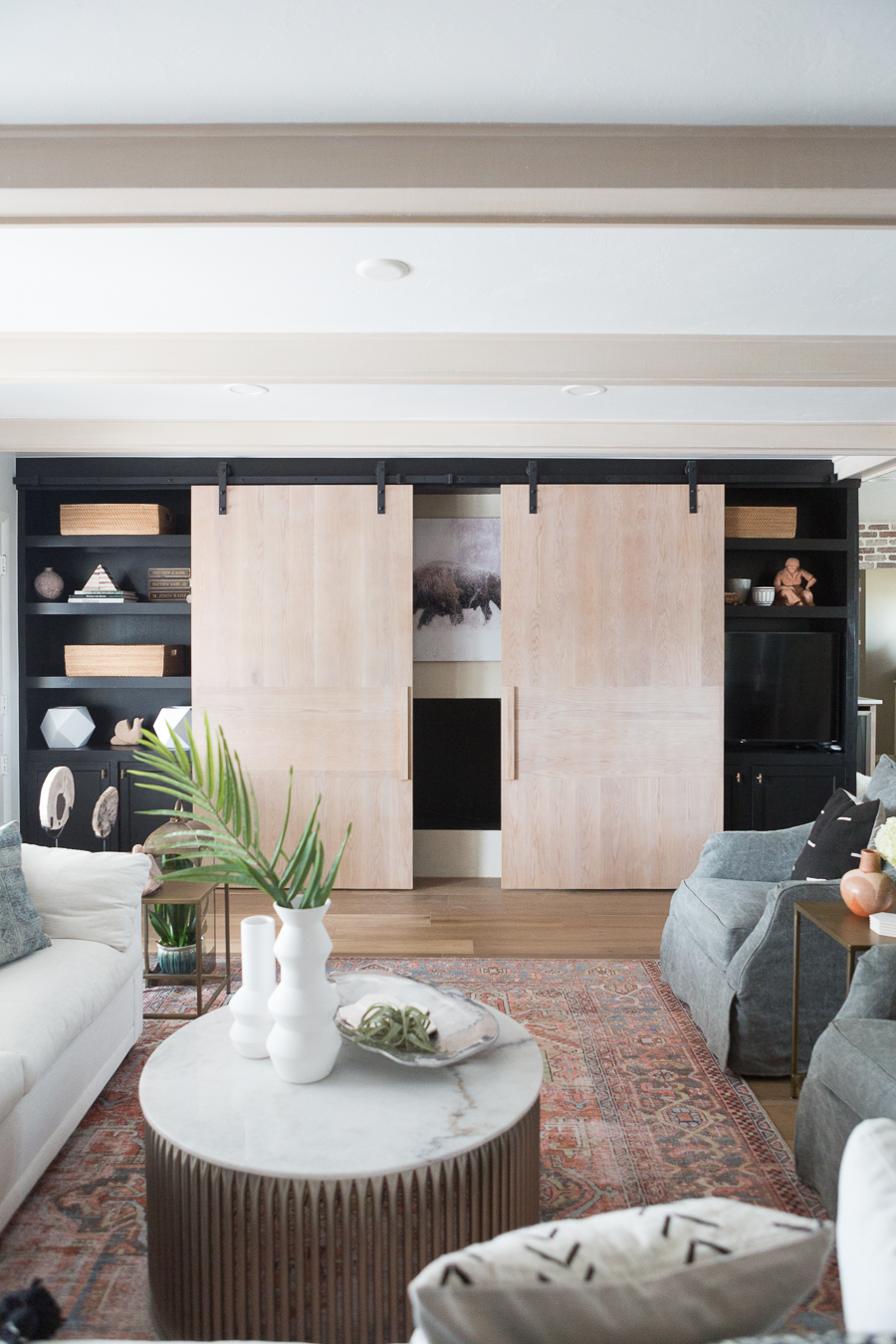 CC and Mike Kane Project Remodel Reveal natural wood sliding barn doors in a living room model with black open shelving