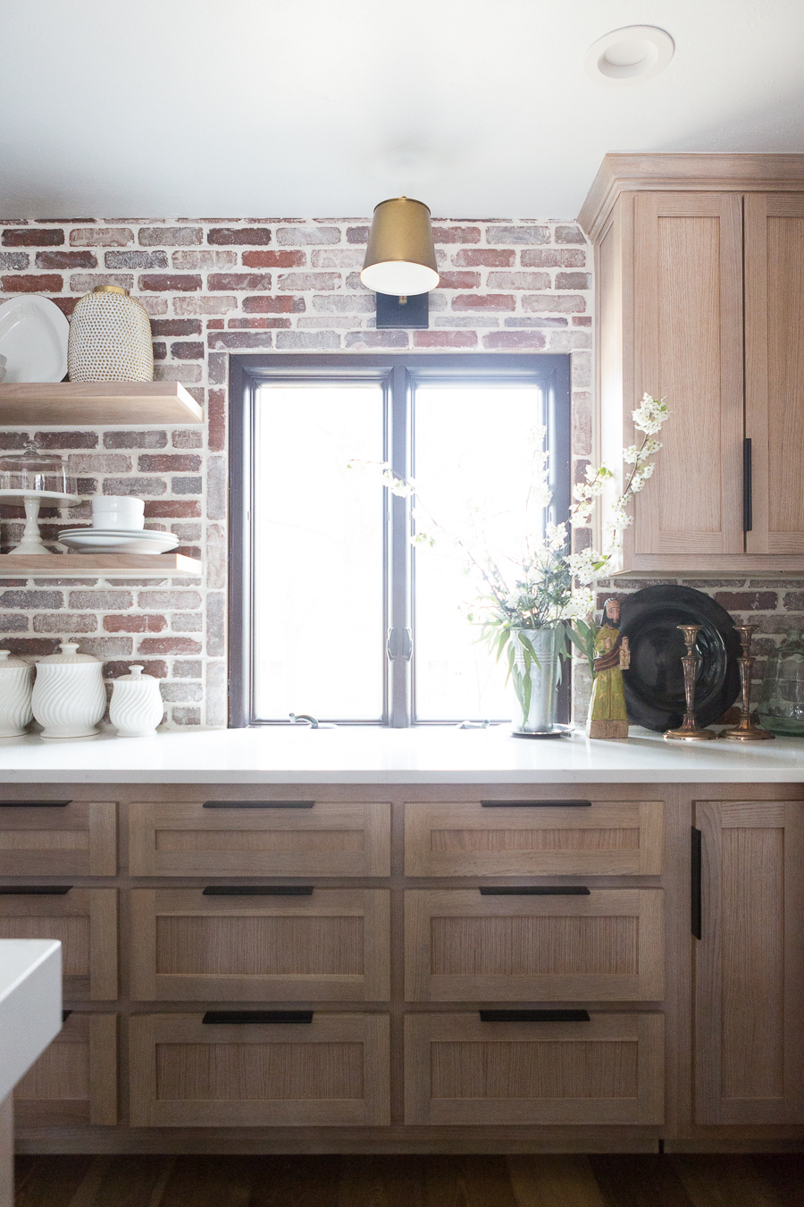 CC and Mike Kane Project Remodel Reveal brick kitchen bacskplash with a white farmhouse sink and black faucet rift sawn white oak cabinets with black hardware