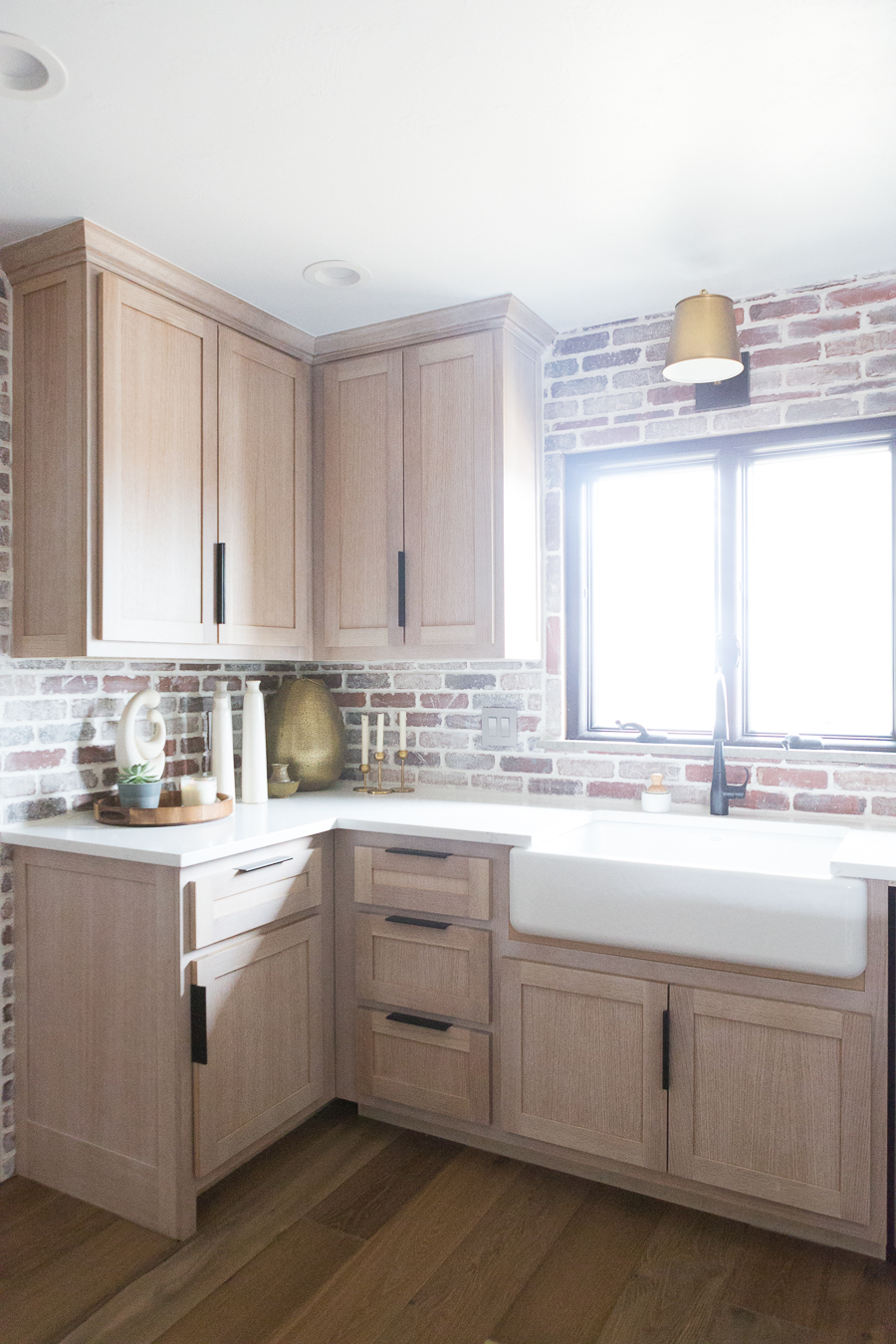 CC and Mike Kane Project Remodel Reveal brick kitchen bacskplash with a white farmhouse sink and black faucet rift sawn white oak cabinets with black hardware