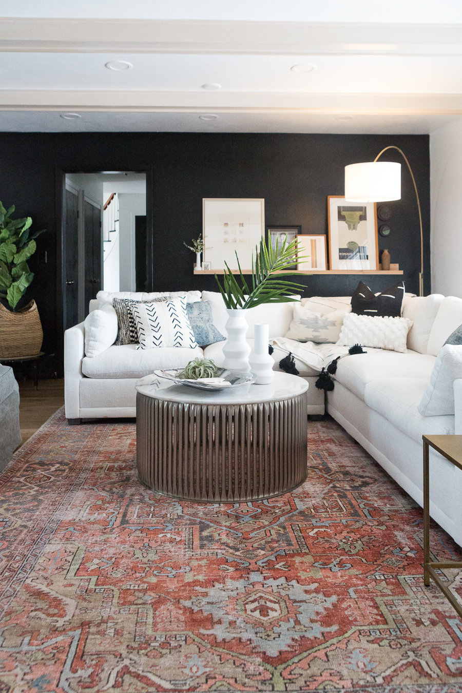CC and Mike Kane Project Remodel Reveal white L shaped sectional on a terracotta loren rug from CC and Mike THE SHOP round coffee table black accent wall with wood art ledge