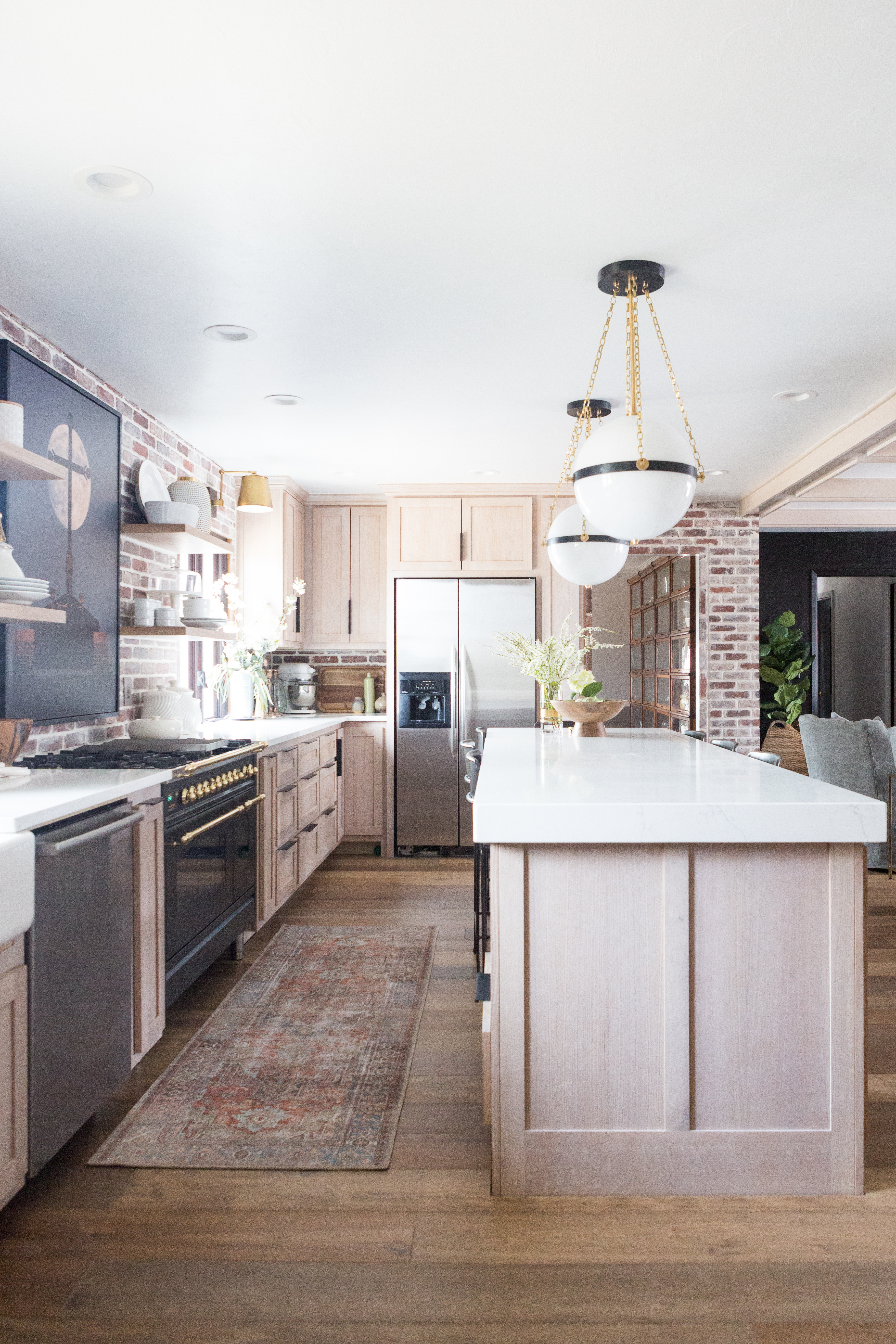 CC and Mike Kane Project Remodel Reveal brick kitchen bacskplash with a white farmhouse sink and black faucet rift sawn white oak cabinets with black hardware