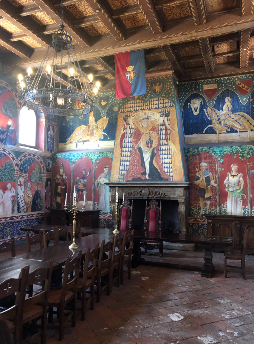 inside the gorgeous castle with long wooden dining tables and multiple colorful murals