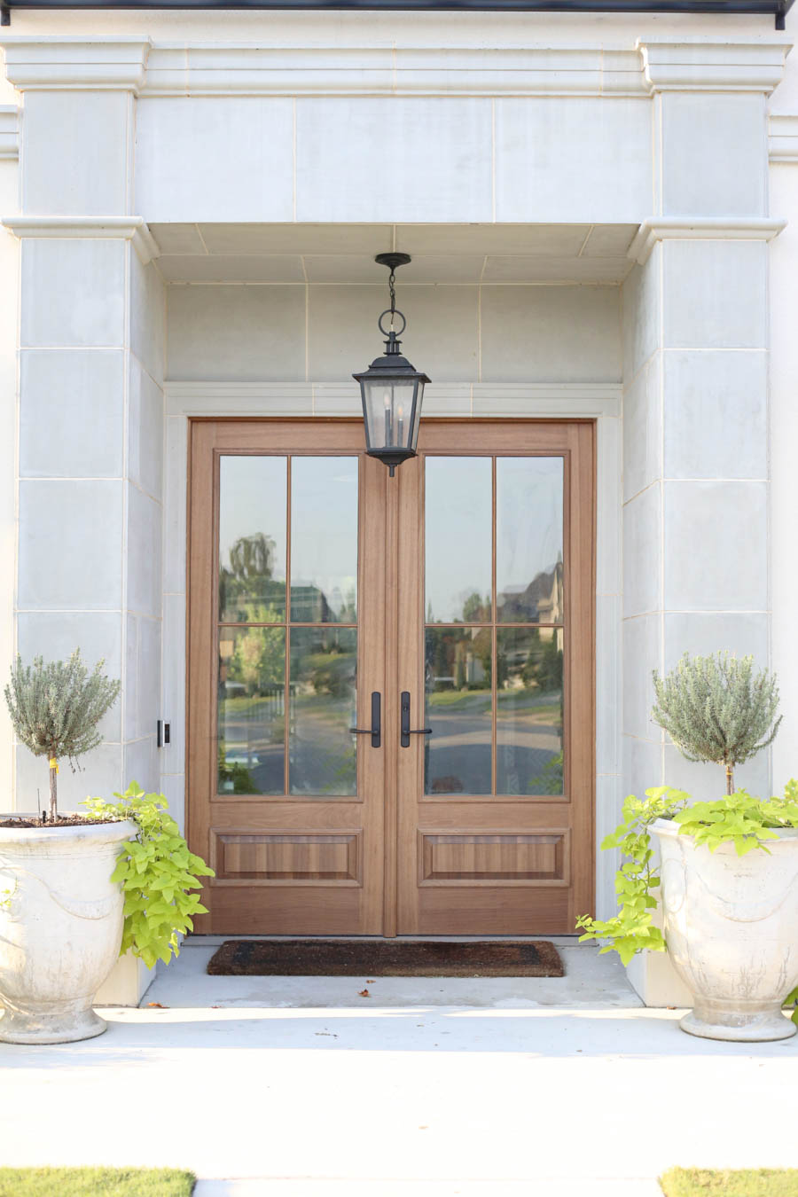 CC and Mike Frisco I Project Reveal-2 white European stucco exterior with cast stone around wooden door and topiary planters beautiful wooden front doors