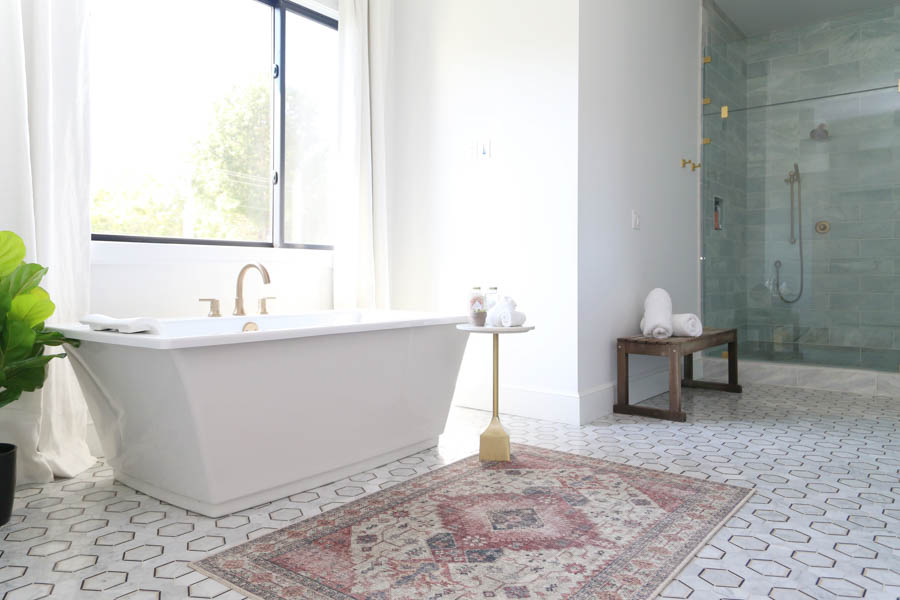 How-to-Update-Your-Rugs-for-Spring pink and gold blush Skye rug on a black and gold  honeycomb marble floor with a large Kohler soaking tub