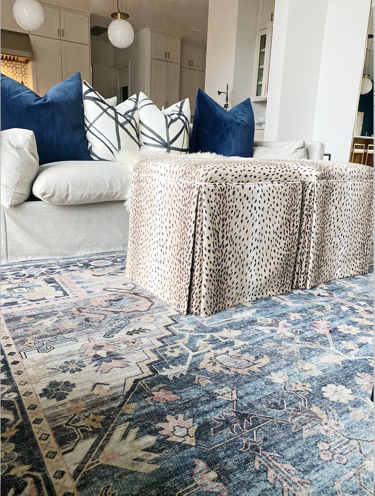 How-to-Update-Your-Rugs-for-Spring  navy Hathaway rug with antelope linen upholstered ottomans in front of a gray slipcovered sofa chair with black and white graphic pillows and navy velvet pillows